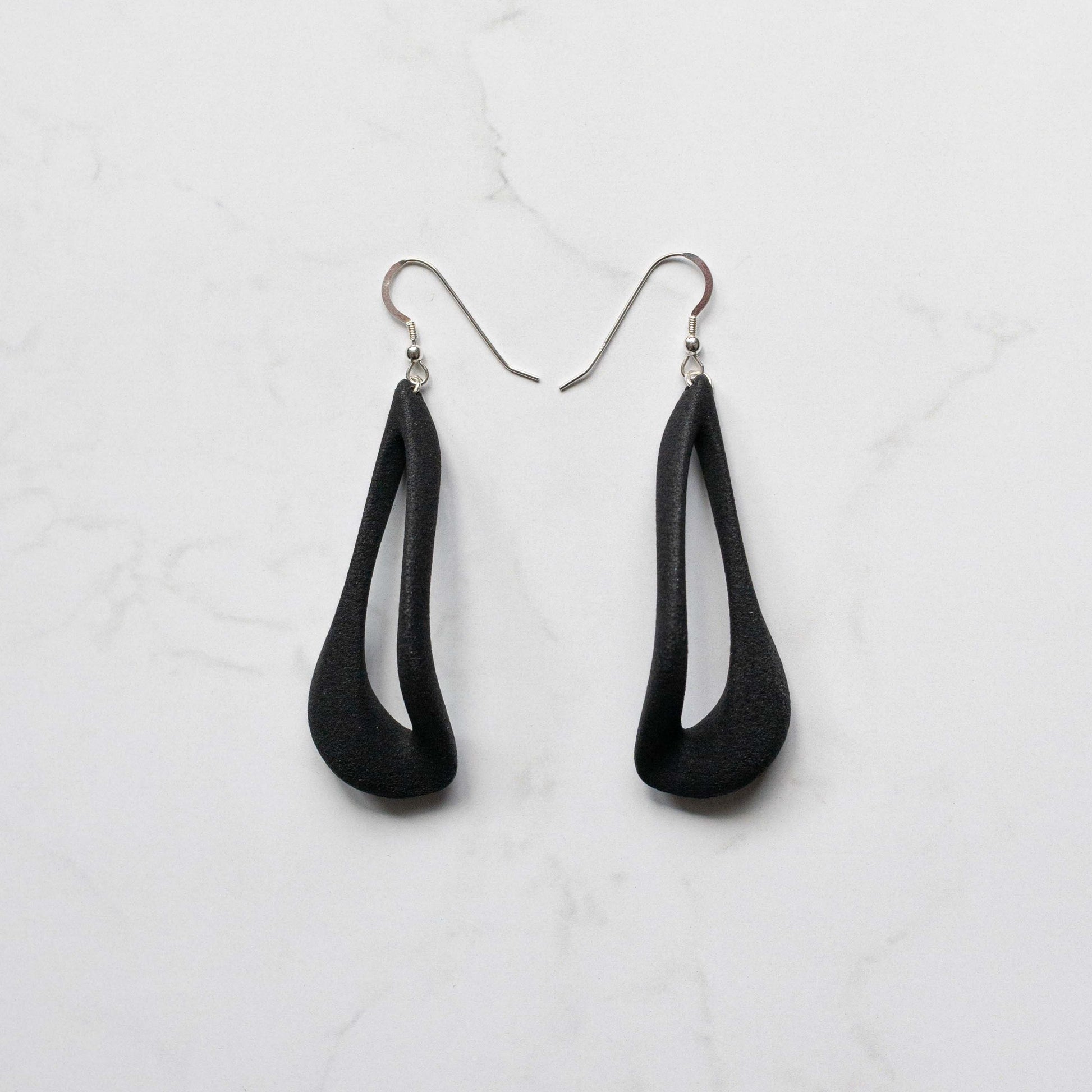 A pair of black teardrop-shaped dangle earrings with silver fishhook wires, displayed on a white marble surface.