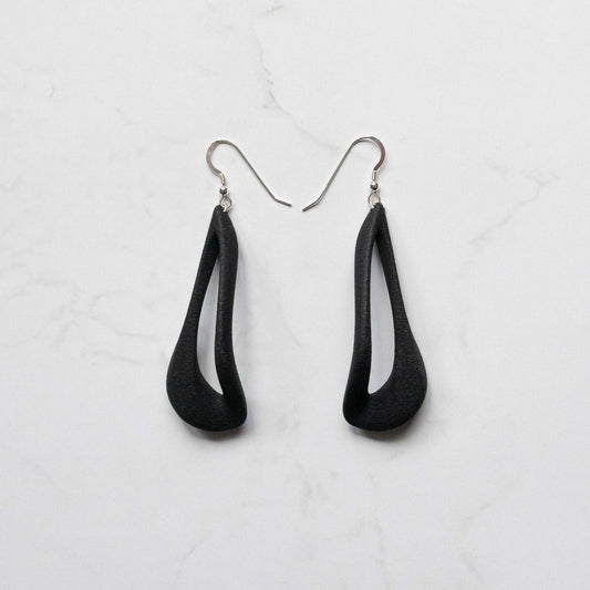 A pair of black teardrop-shaped dangle earrings with silver fishhook wires, displayed on a white marble surface.